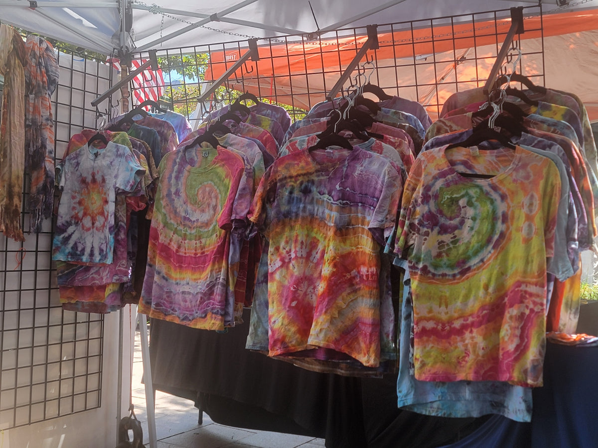 Colorful tie-dye shirts displayed under a canopy tent